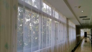 A corridor with large windows covered by sheer curtains, allowing natural light to enter. - Hua Nan Business Hotel (Guangzhou)