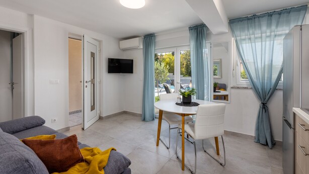 A modern living room with a sofa, a dining table, and a TV mounted on the wall. - Villa Dubravka A (Crikvenica)