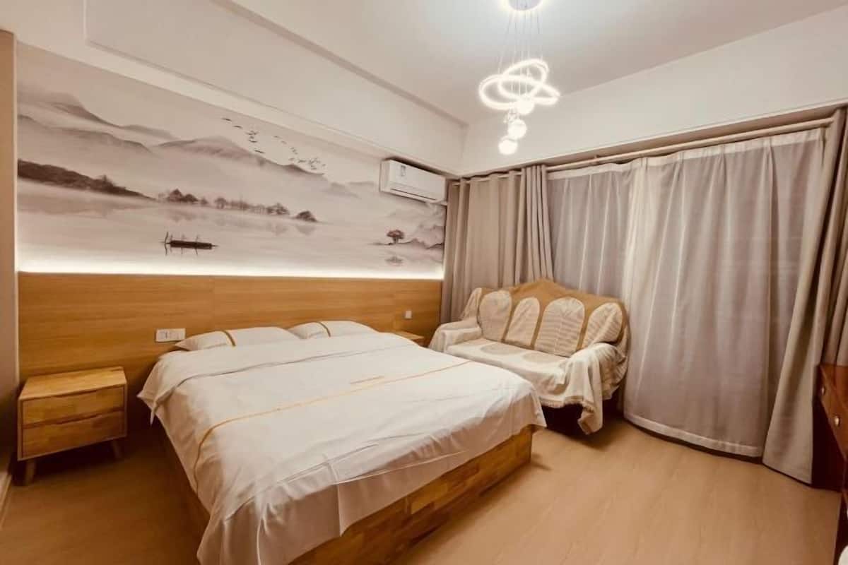 A bedroom with a wooden headboard, a bed with white bedding, a bedside table, a wall-mounted air conditioner, and a large window with curtains.