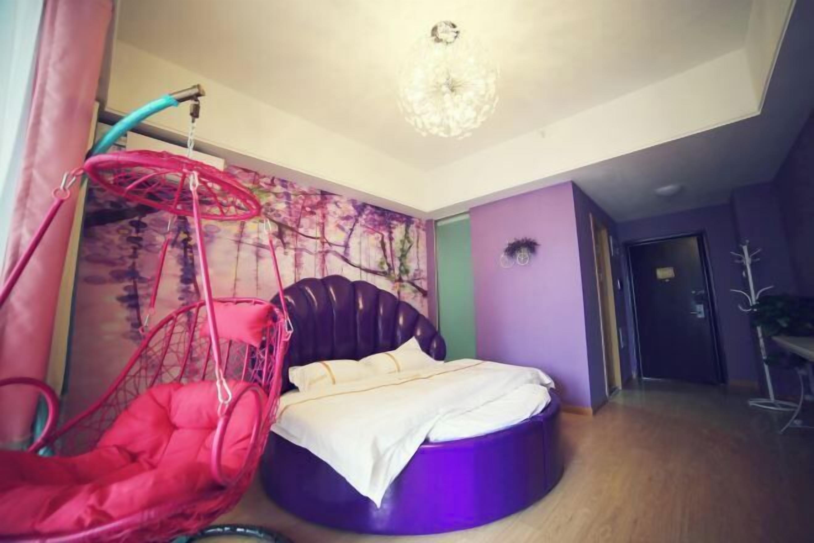 A room with a round bed, a hanging chair, and a wall with abstract art.