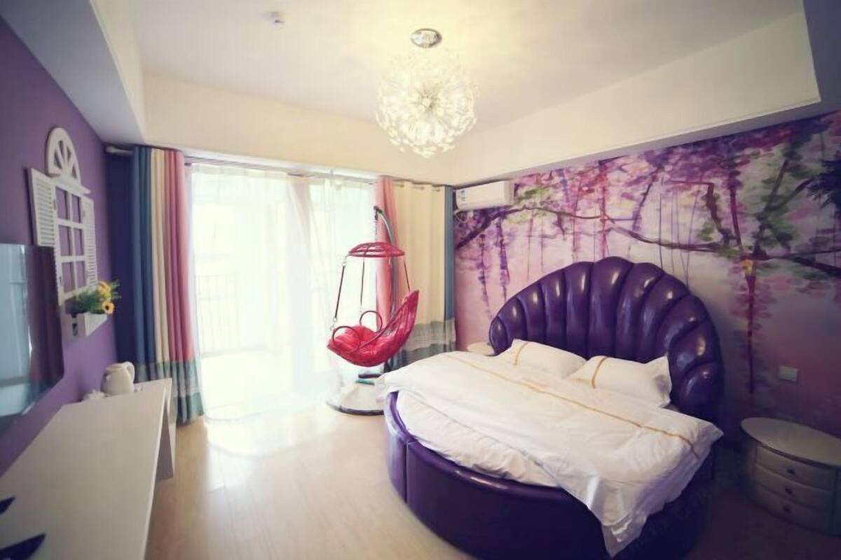 A bedroom with a large bed, a hanging chair, a desk, and a wall mural.