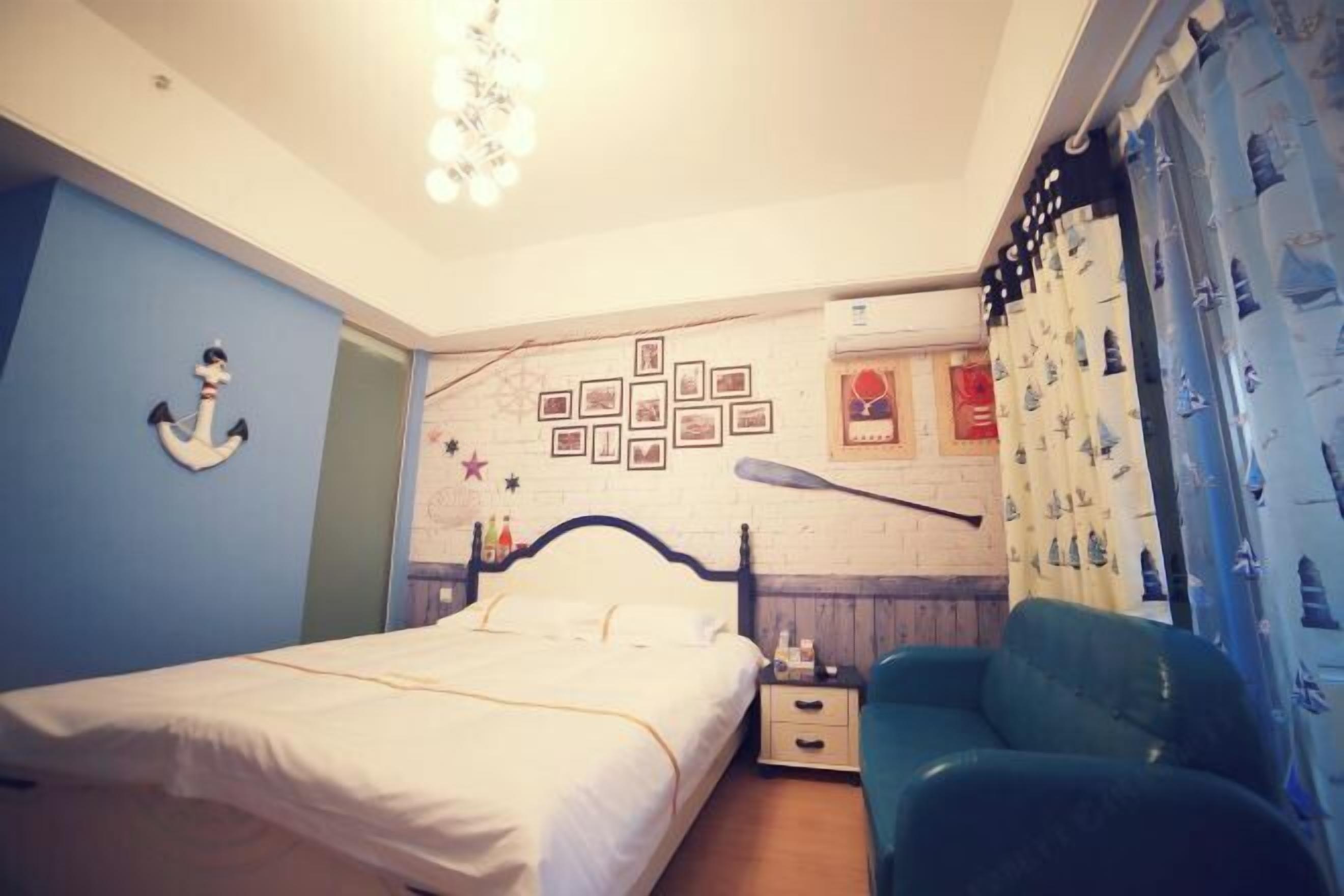 A bedroom with a bed, a nightstand, a green chair, a wall with pictures, and a curtain with a nautical pattern.