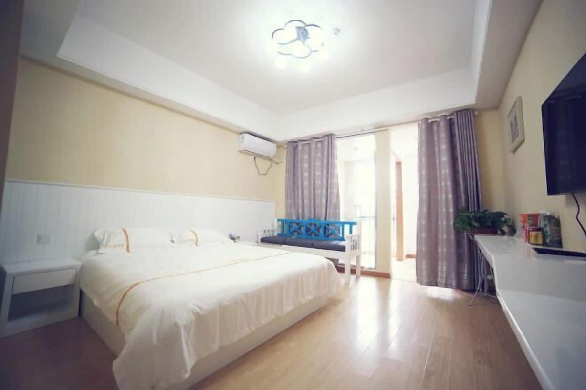 A hotel room with a bed, a desk, a chair, a TV, and an air conditioning unit.