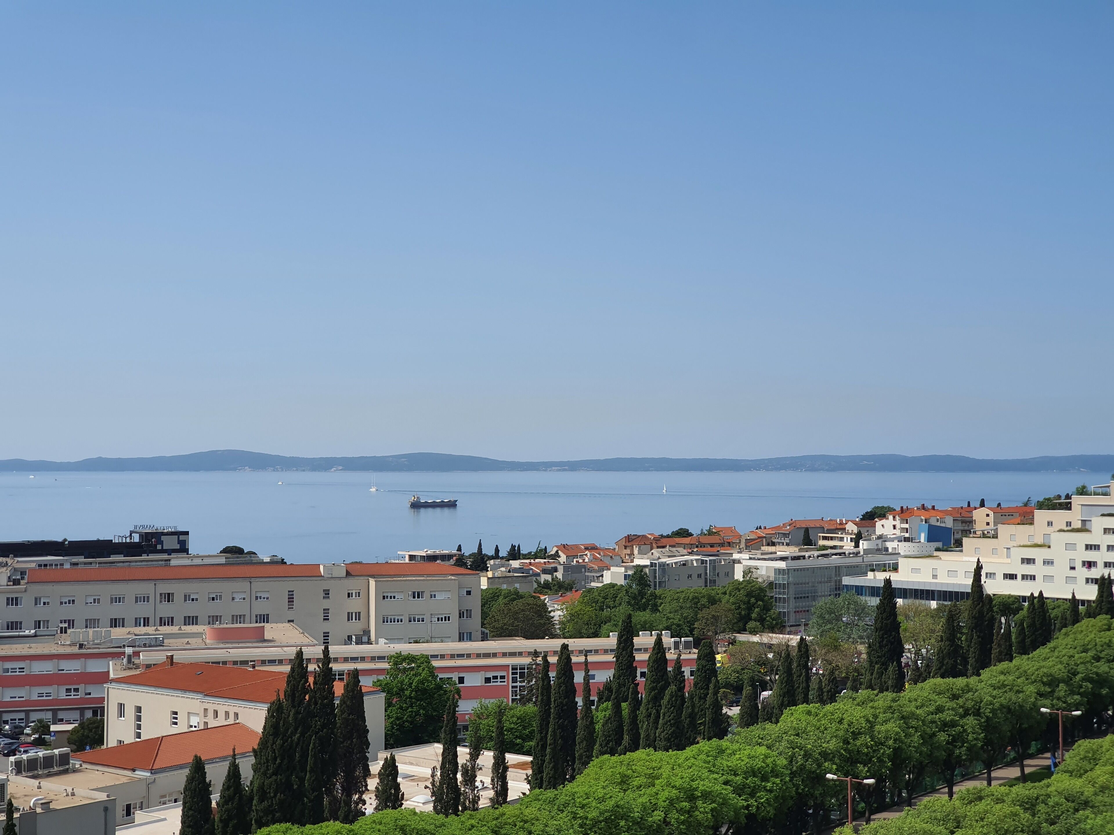 A coastal cityscape with buildings, trees, and a clear view of the sea.