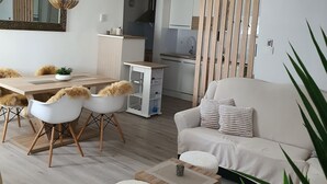 Ett modernt vardagsrum med en soffa, ett soffbord och en matplats med stolar. I bakgrunden syns ett kök.