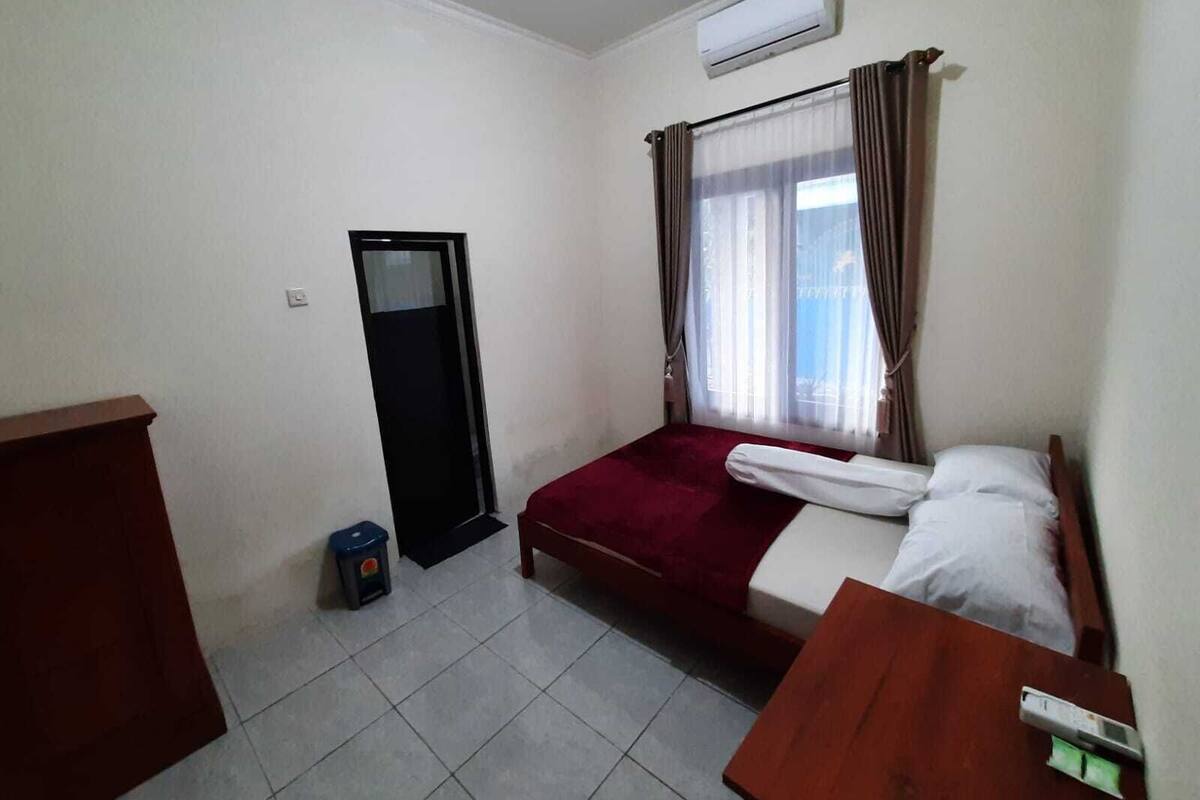 A small, clean room with a bed, a desk, a mirror, and an air conditioning unit.
