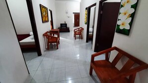 A hallway with a tiled floor, wooden chairs, a small table, and a television. - 999 KHS Homestay (Banyuwangi)