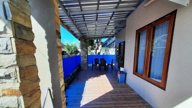 A covered outdoor area with a wooden floor, a stone wall, and a blue fence. - 999 KHS Homestay (Banyuwangi)