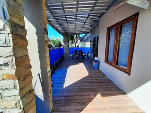 A covered outdoor area with a wooden floor, a stone wall, and a blue fence.