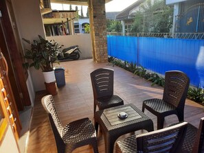 A patio with wicker furniture, a potted plant, and a blue fence.