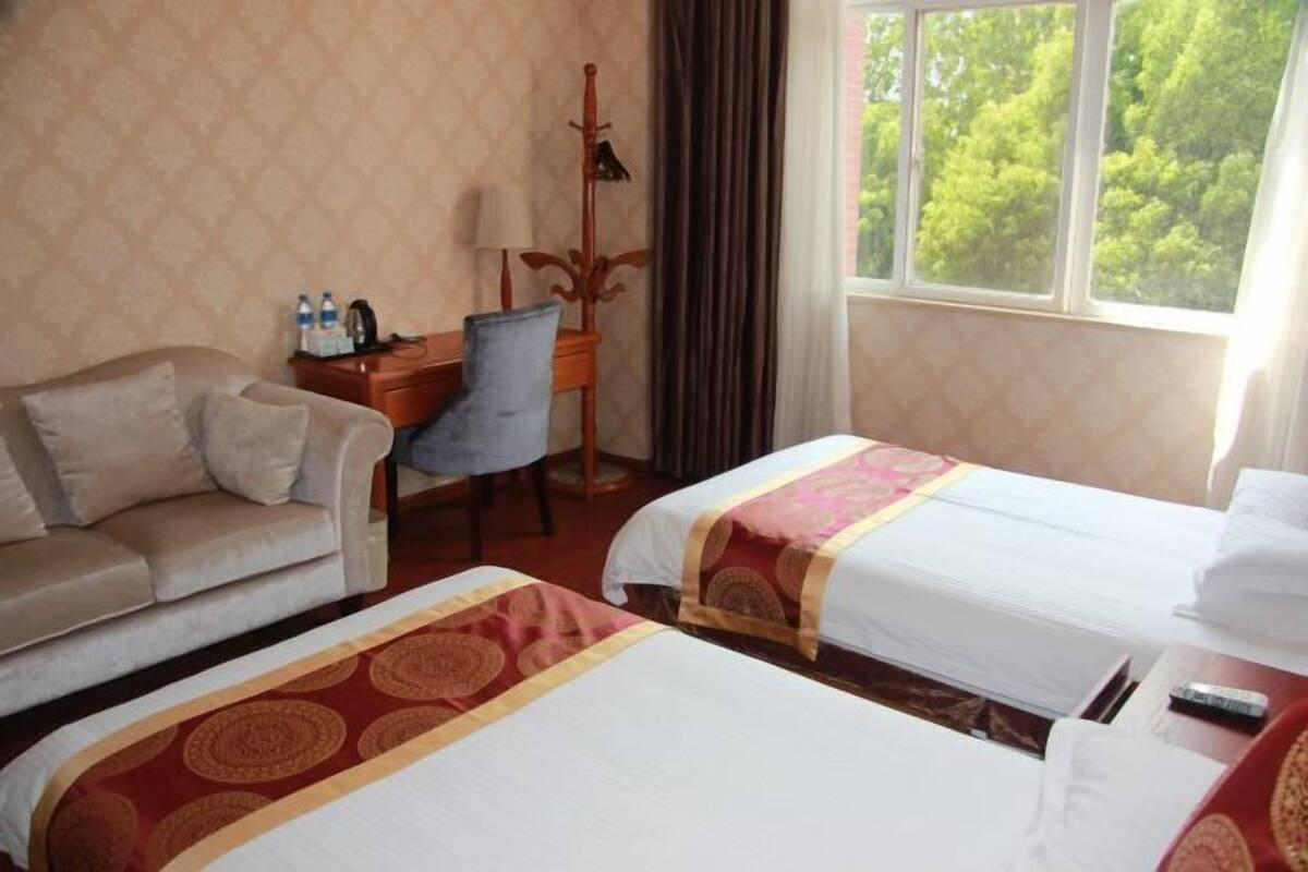 A hotel room with two beds, a sofa, a desk, and a window with a view of trees.