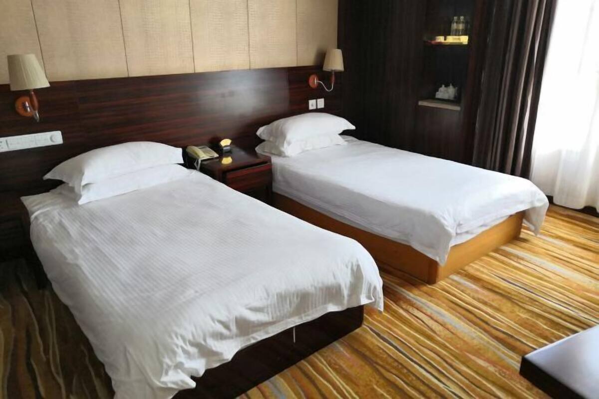 A hotel room with two single beds, wooden headboards, bedside lamps, a nightstand with a phone, and a striped carpet.