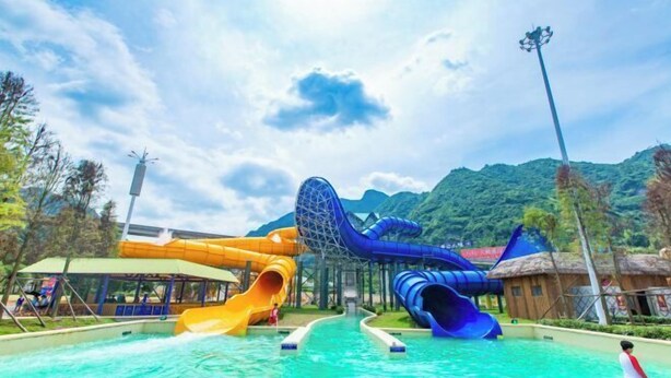 Un parc aquatique doté de deux toboggans, d’une piscine et d’un paysage montagneux en toile de fond.