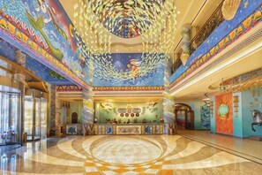 Un hall d’entrée avec un comptoir de réception central, un grand motif circulaire au sol et un plafond orné d’une fresque représentant des poissons.