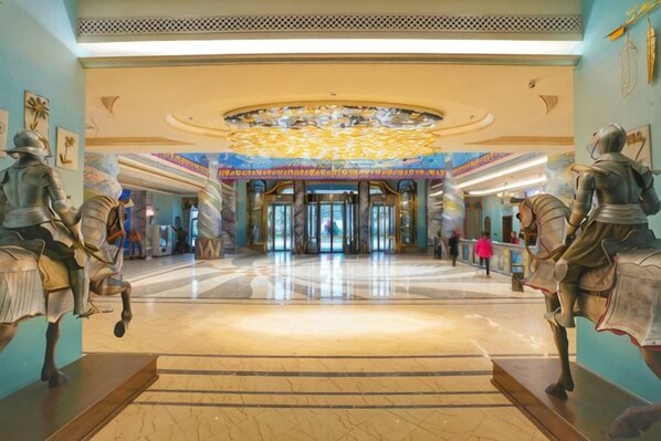 A grand lobby with a central chandelier, a marble floor, and statues of armored figures.