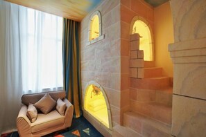 Ein gemütliches Wohnzimmer mit einem beigen Sofa, einem Kamin aus Stein mit Rundbogenfenstern und einer Treppe, die zu einer oberen Ebene führt.