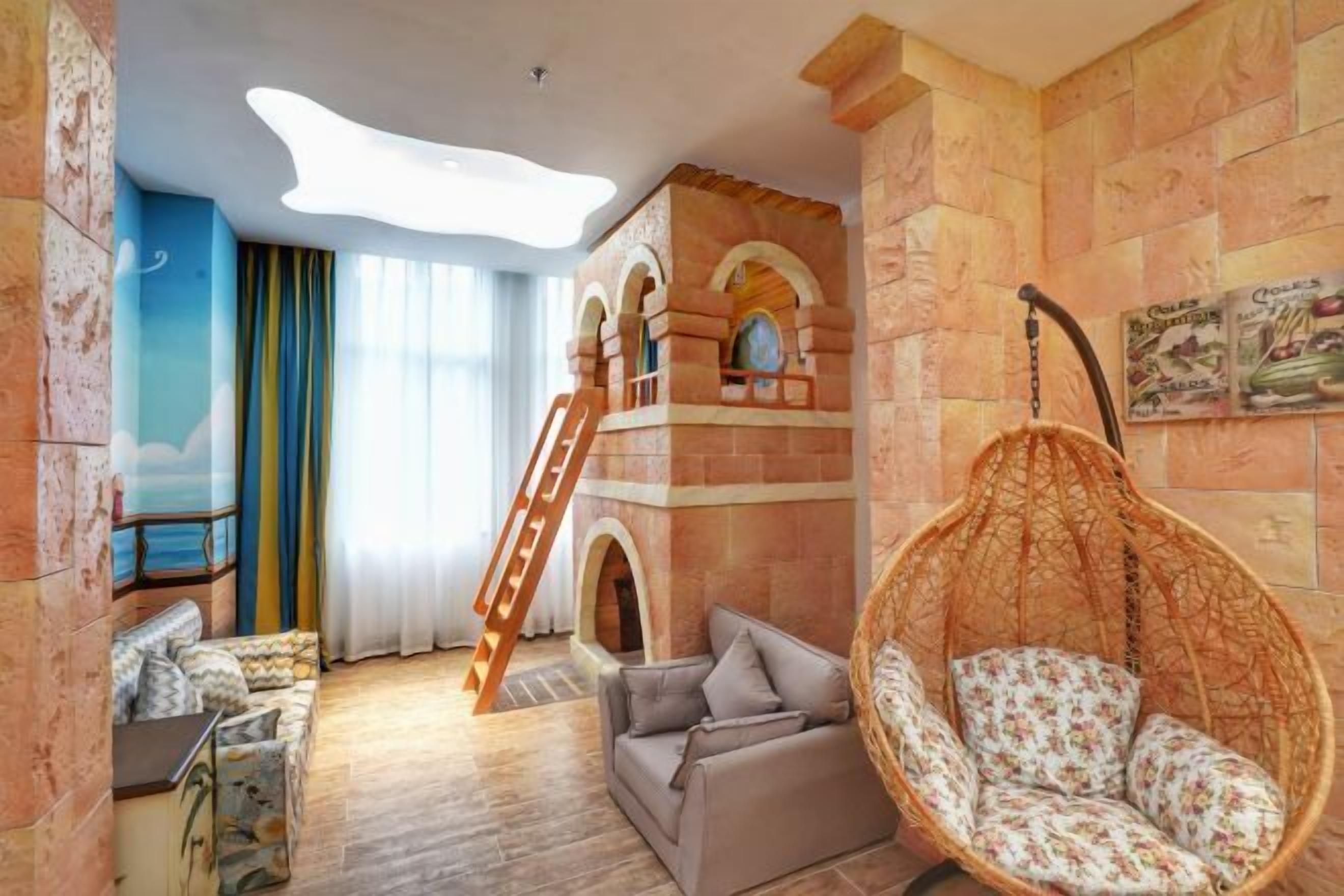 A room with a sofa, a hanging chair, a ladder, and a stone wall with arched windows.