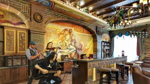 Un espace bar agrémenté d’une fresque murale, d’un comptoir, de tabourets et d’un homme jouant de la guitare.