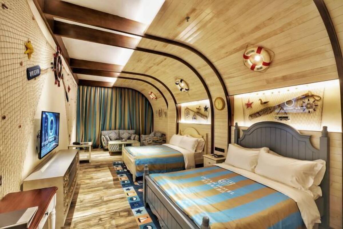 Ein Hotelzimmer mit zwei Betten, einem Fernseher, einem Schreibtisch und einer Wanduhr.