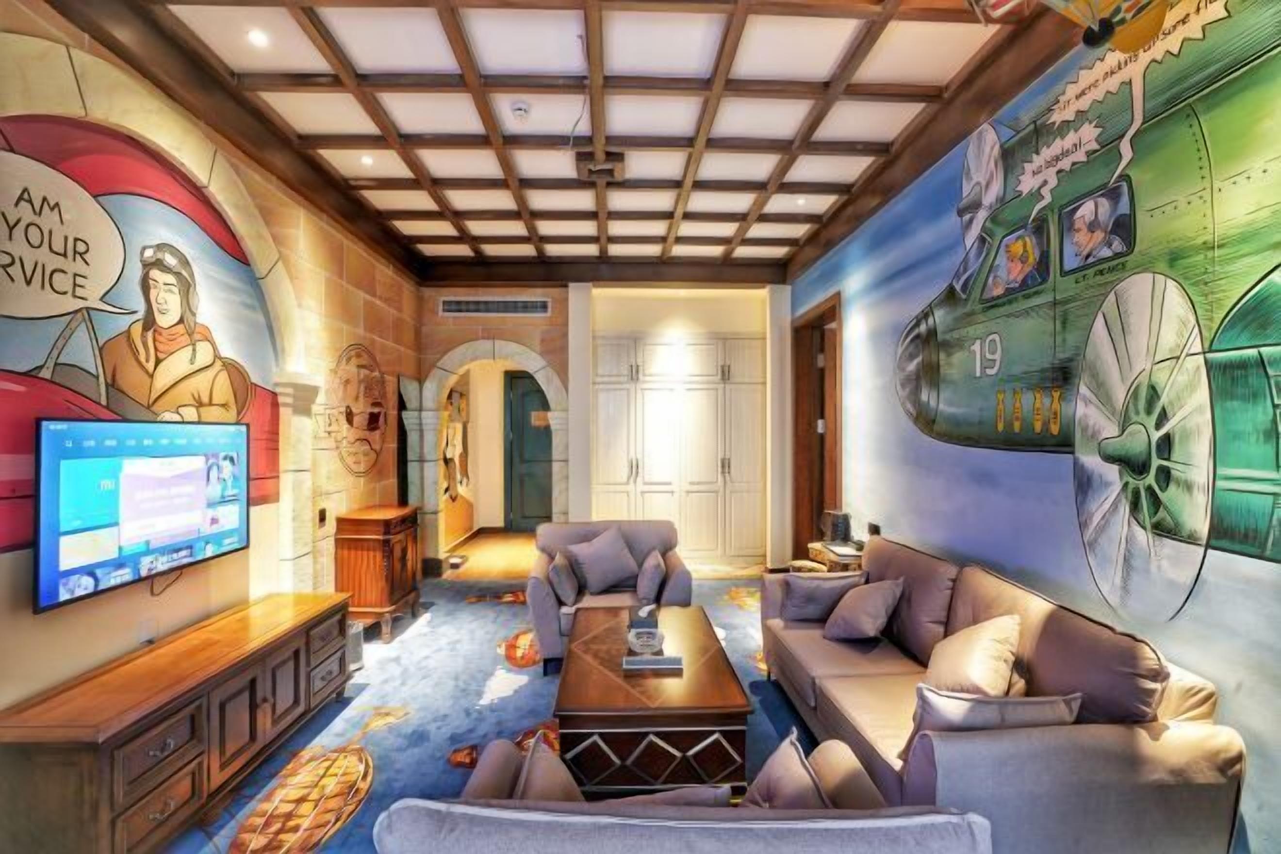 A room with a television, sofas, a coffee table, and a mural of a fighter jet.