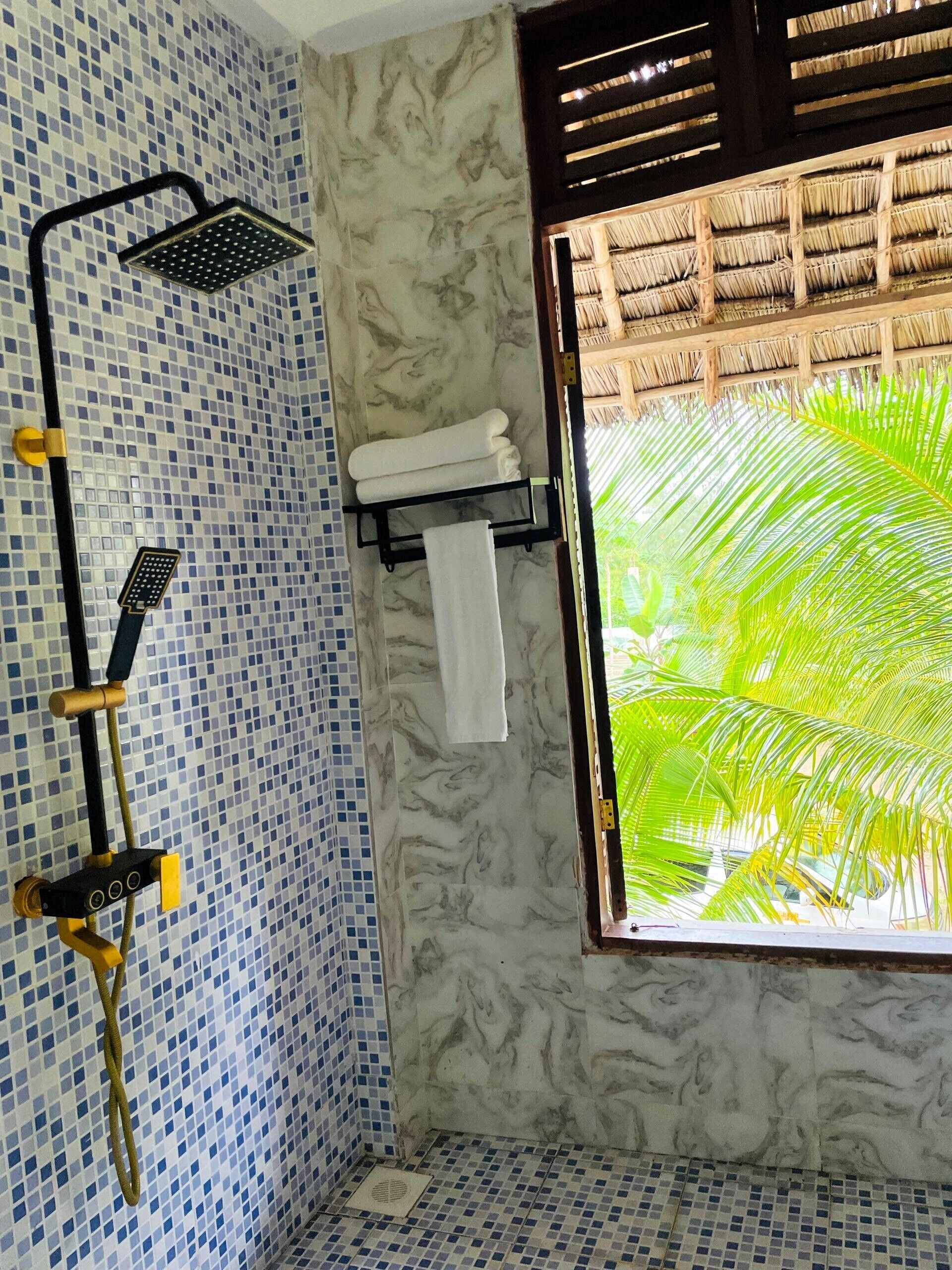Un bagno con doccia, asciugamano e finestra vista palme.