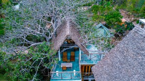 A treehouse with a thatched roof, multiple levels, and a balcony.