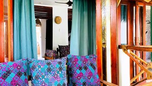 A room with a wooden-framed sofa with patterned cushions, a thatched roof, and a view of the interior.