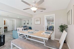 A dining area with a table set for four, a ceiling fan, and a view into the adjacent living room.