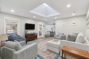 A spacious living room with a skylight, a flat-screen TV, and a dining area with a table and chairs.