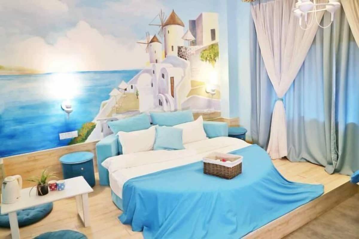 A bedroom with a bed, bedside tables, a nightstand, a window with curtains, and a mural of a coastal scene.