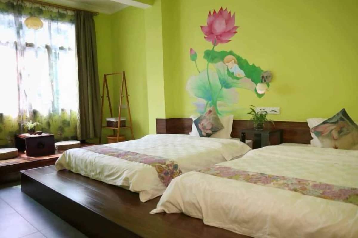 A hotel room with two beds, a painting of a lotus flower, a wooden floor, and a window with curtains.