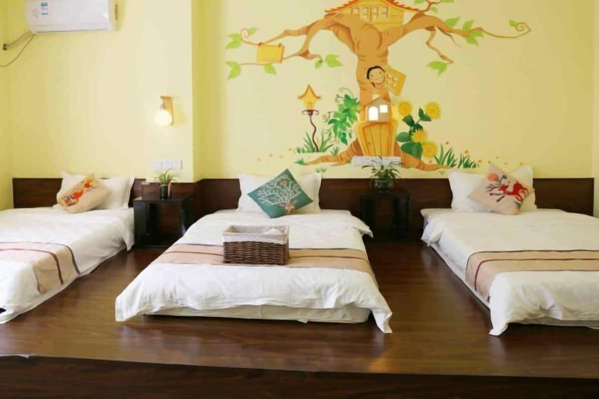 A hotel room with three beds, a large mural on the wall, and a wooden floor.