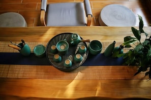 Ein Holztisch mit einer Tablett voller grüner Teekannen und Tassen, einer Pflanze und einer Tischmatte.