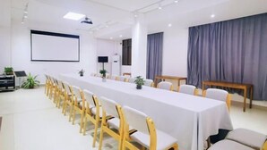Una sala de conferències amb una taula llarga, cadires, una pantalla de projector i un gran finestral amb cortines.