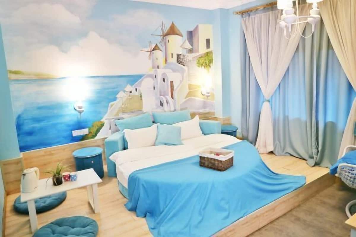 A bedroom with a bed, a nightstand, a lamp, and a view of a painted coastal scene.