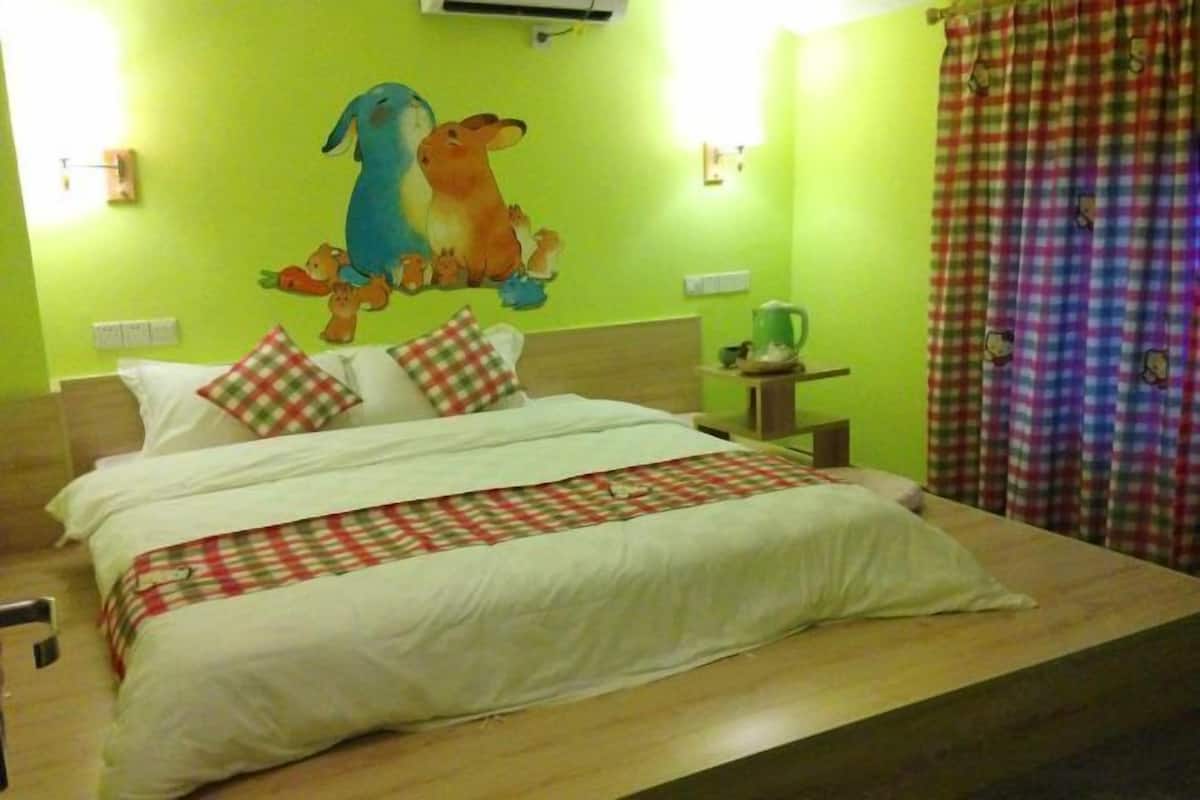 A bed with a checkered blanket, a wall with a cartoon mural, a small table with a green object, and a checkered curtain.