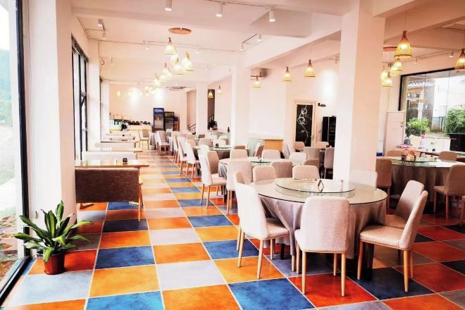 A hotel dining area with round tables and chairs, a colorful checkered floor, and large windows.