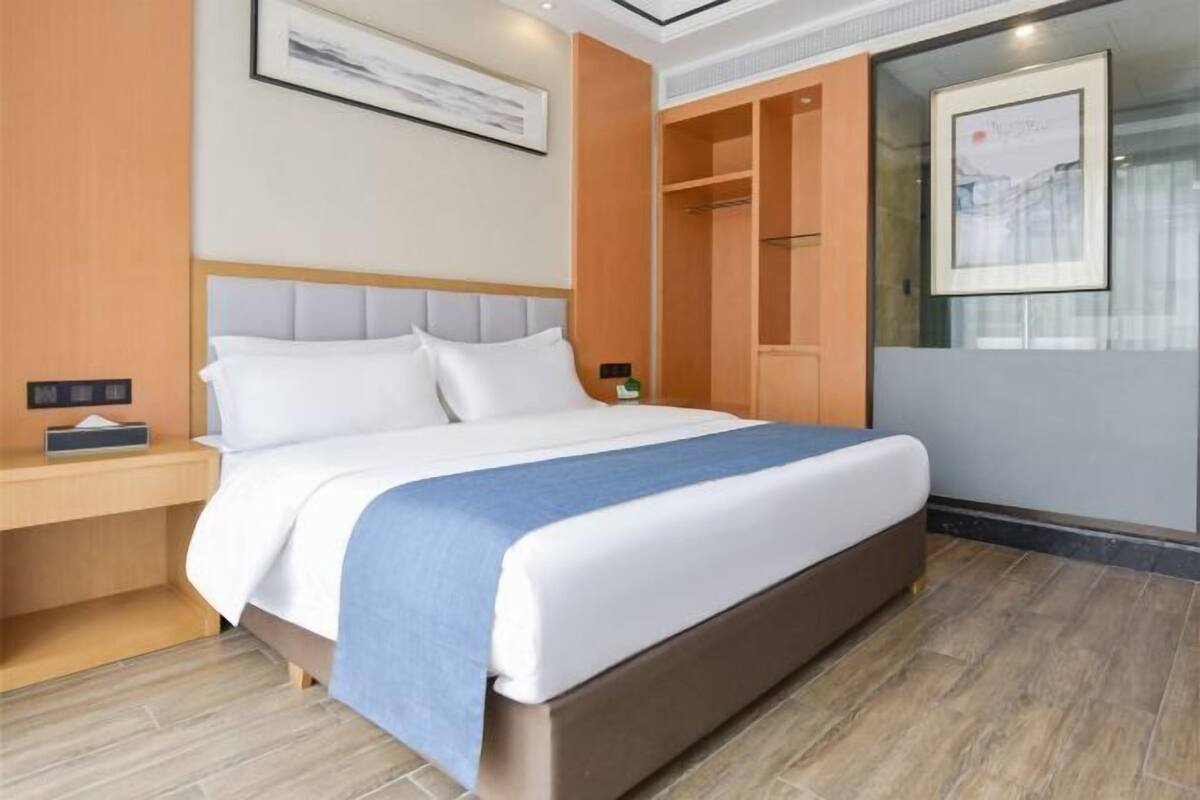 Ein Hotelzimmer mit Bett, Nachttisch, Kleiderschrank und einem gerahmten Bild an der Wand.