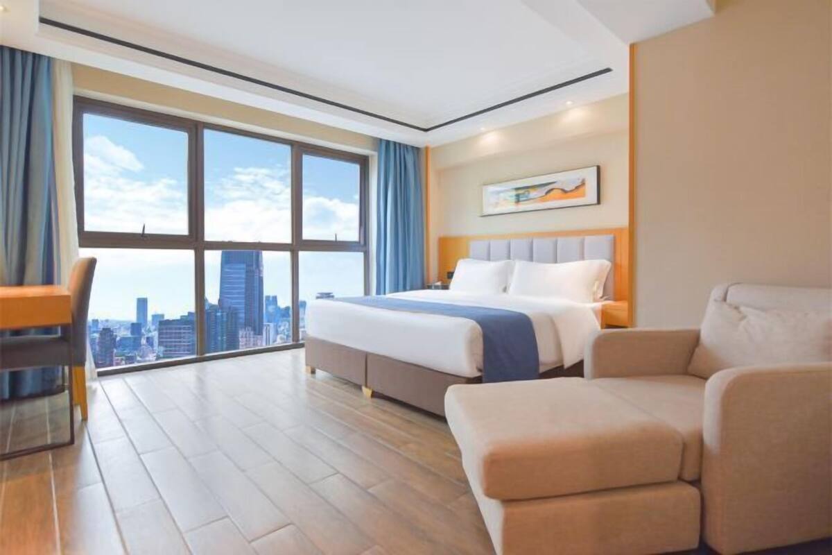 Ein Hotelzimmer mit großem Fenster, einem Bett, einem Schreibtisch und einem Sessel.