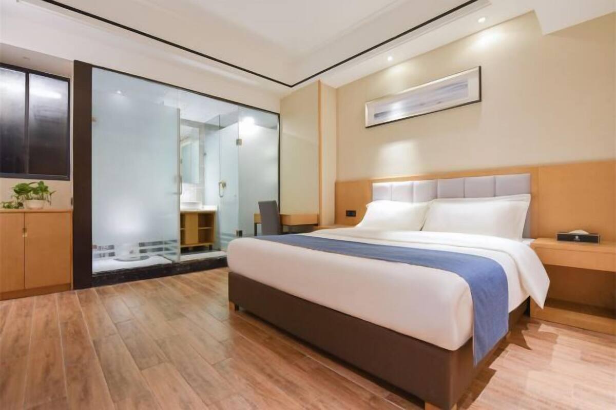 Ein modernes Hotelzimmer mit einem großen Bett, einer Duschkabine aus Glas und einem Holzboden.