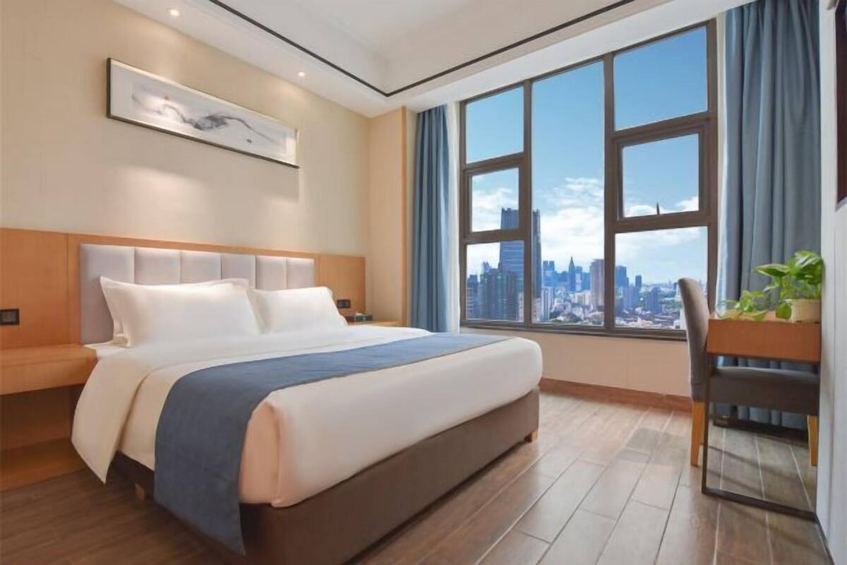 Ein modernes Hotelzimmer mit einem großen Bett, Blick auf die Stadt, einem Schreibtisch und einem Stuhl.