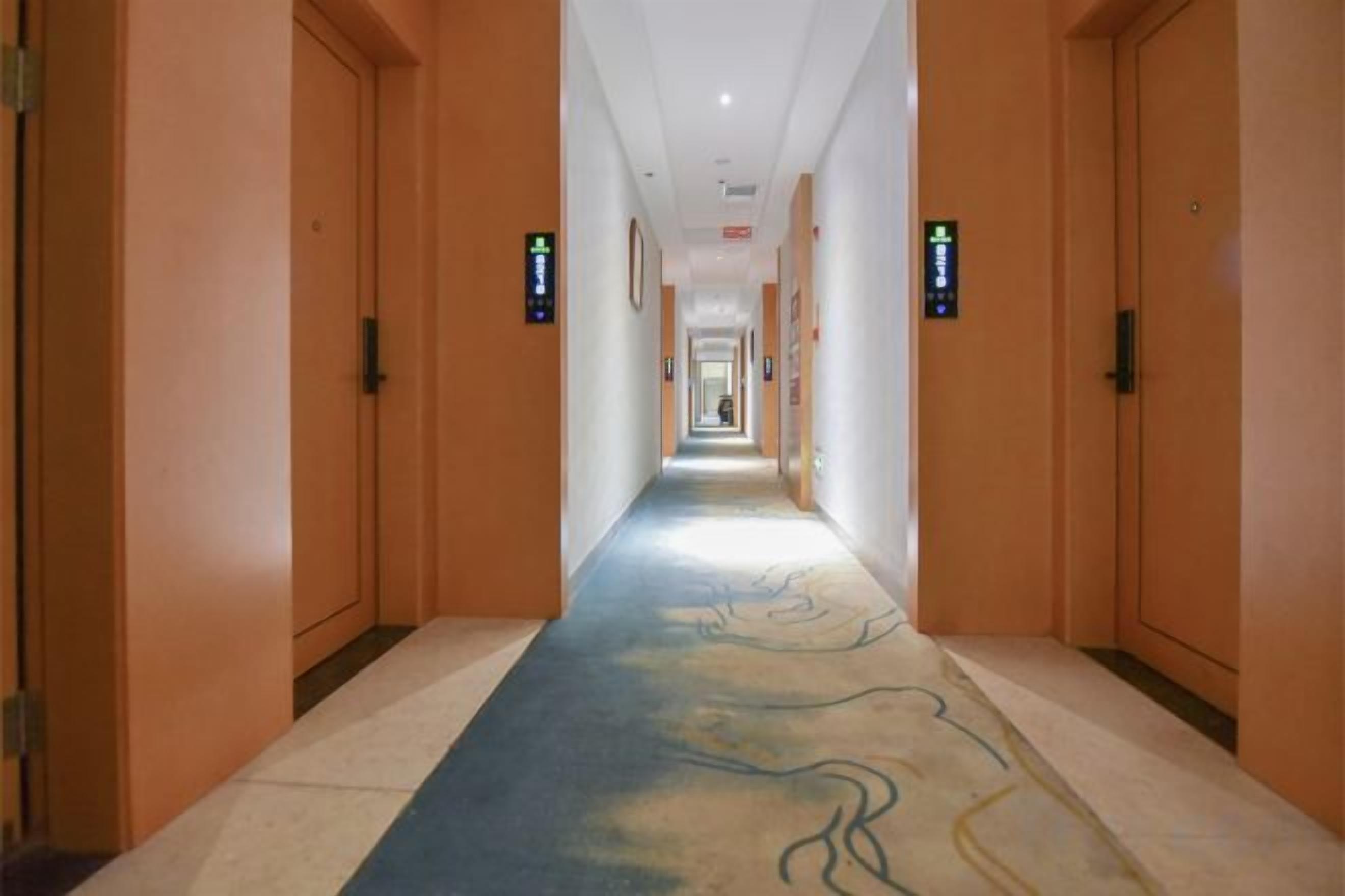 A hotel corridor with doors on both sides, a carpeted floor, and directional signs on the walls.
