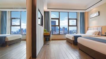 A hotel room with two beds, a desk, and large windows offering a city view.