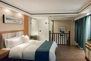 Habitación de hotel con una cama grande, cabecera de madera, mesita de noche, escritorio, espejo y vista al pasillo.