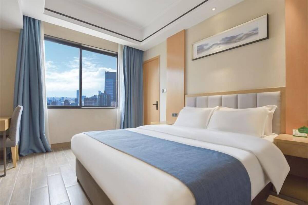 Ein modernes Hotelzimmer mit einem großen Bett, einem Schreibtisch und einem Fenster mit Blick auf die Stadt.