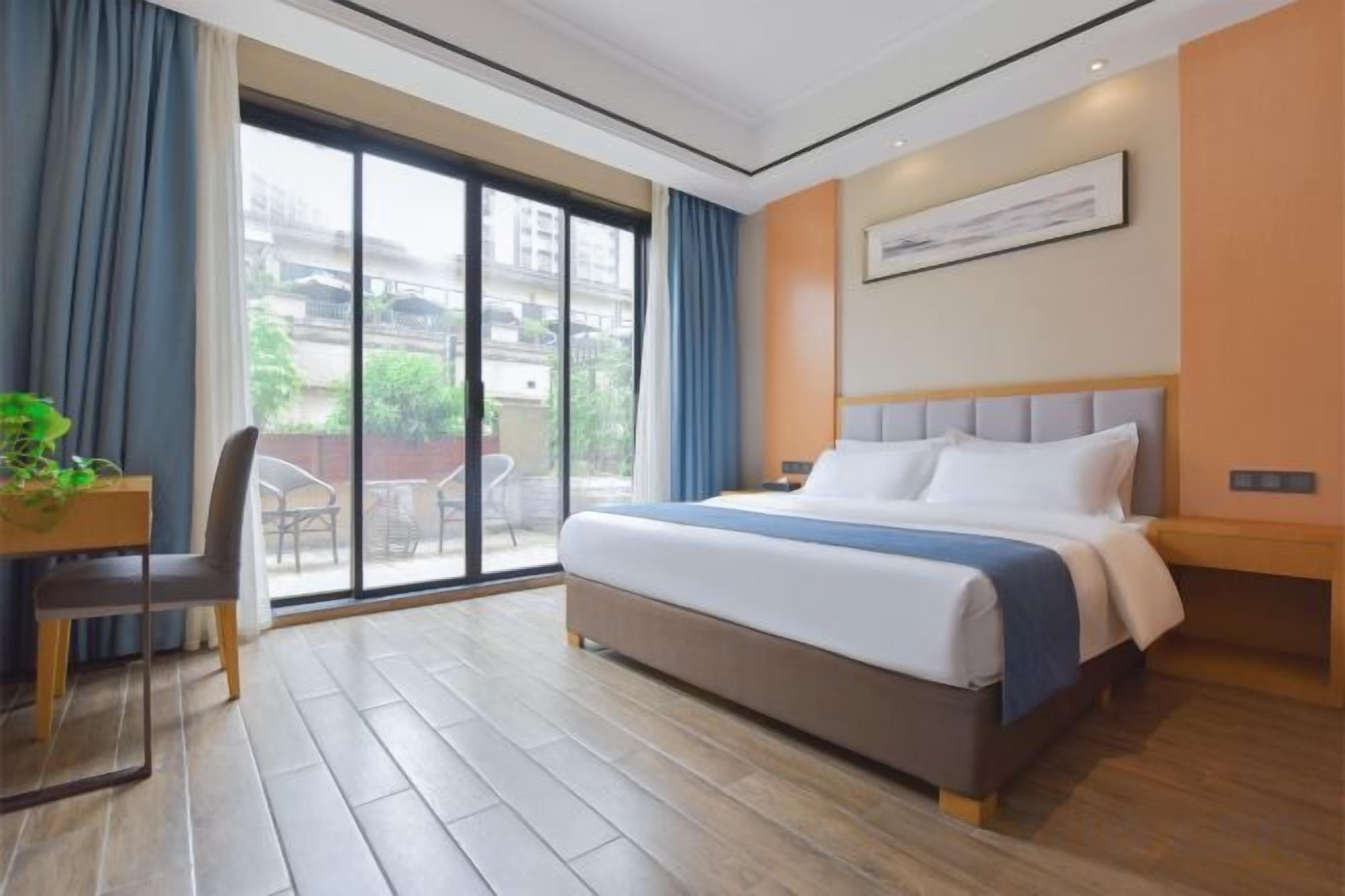 Habitación de hotel con una cama grande, un escritorio con silla y vistas a través de un ventanal corredero.