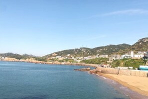 A coastal view with a sandy beach, calm sea, and a hillside with buildings. - Qingwu Fisherman's Hostel (Shengsi)