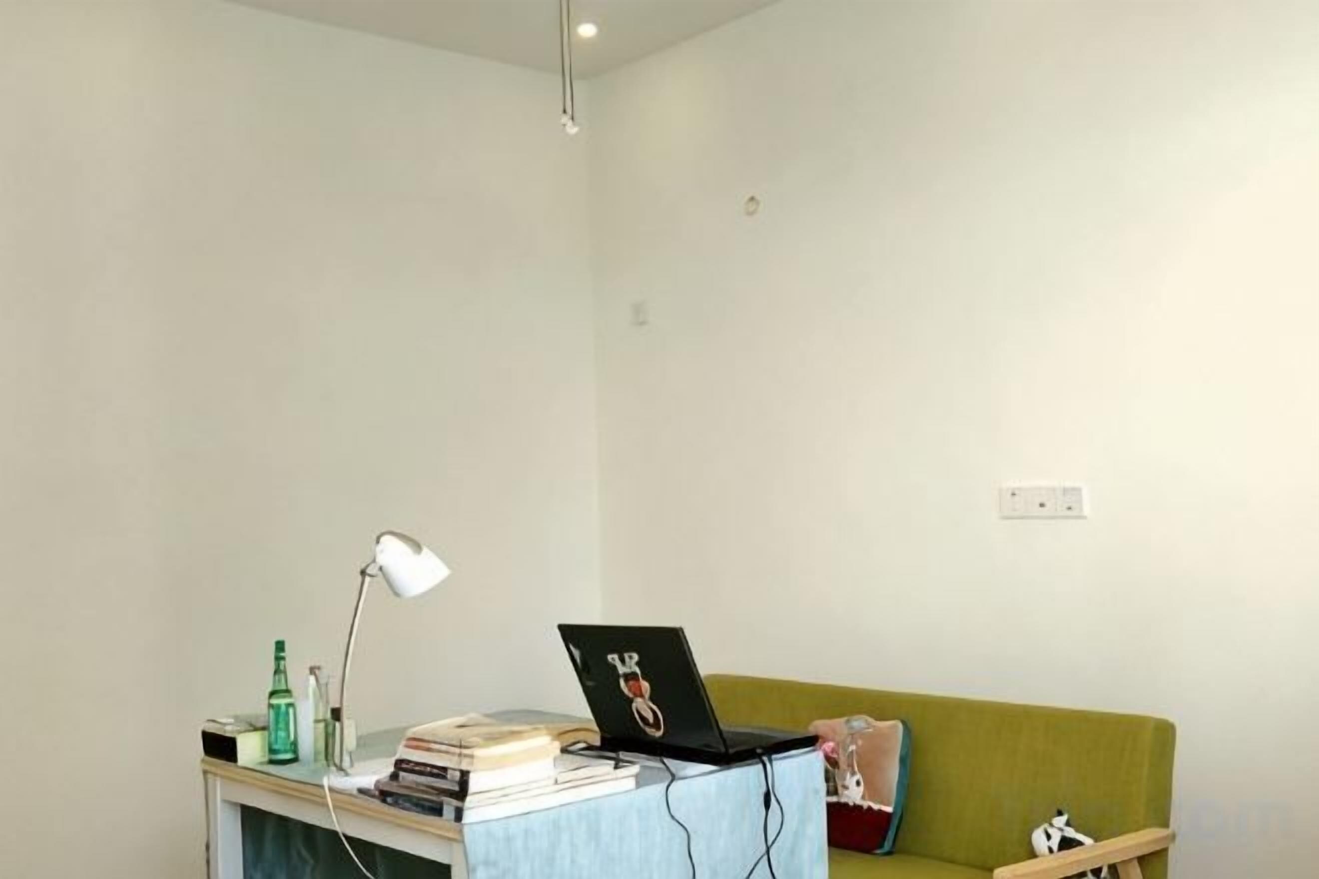 A room with a desk, a laptop, a lamp, a couch, and a small shelf.