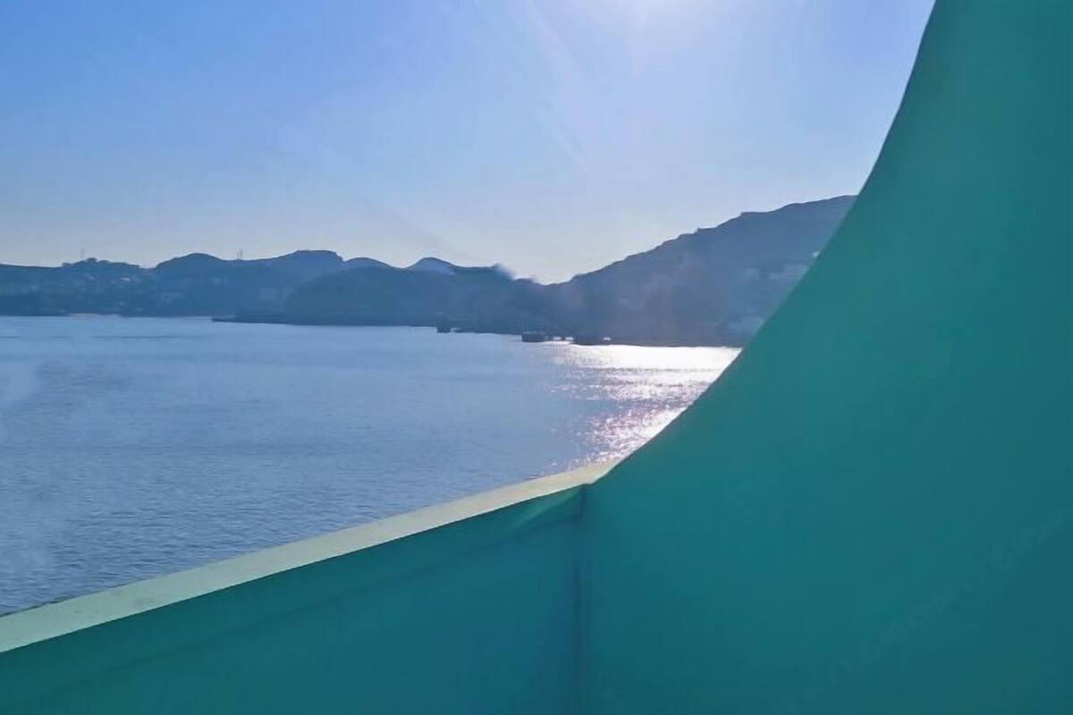 A coastal view with a clear sky, calm water, and distant hills.