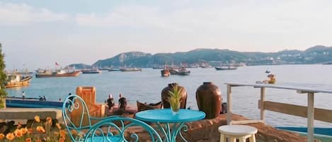 A waterfront patio with outdoor seating, overlooking a harbor with boats.
